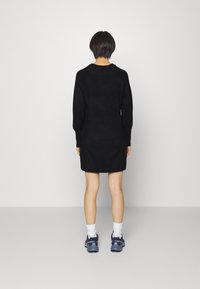 Svart stickad klänning med lång ärm, rund halsringning, strukturerad tyg och en lös passform, matchad med marinblå sneakers och vita strumpor.