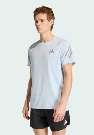 Camiseta deportiva azul claro con mangas cortas, cuello redondo y tres franjas grises en el hombro izquierdo. Corte estándar.