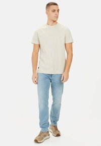 Beżowa bawełniana koszulka z krótkim rękawem, zestawiona z jasnoniebieskimi dżinsami i szaro-brązowymi trampkami. Prosty design, bez wzorów i akcentów.