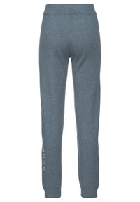 Grijze, strakke joggingbroek met een elastische tailleband, taps toelopende pijpen en witte tekst "SAND" aan de linkerkant. Zacht materiaal en gladde textuur.