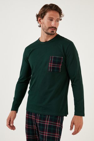 Chemise verte à manches longues avec une poche à carreaux ; en coton. Portée avec un pantalon à motifs à carreaux dans des couleurs sombres, avec des accents rouges et verts.