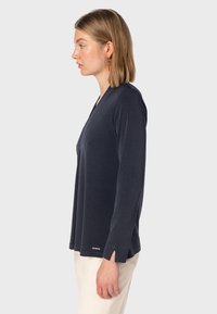 Maglietta a maniche lunghe blu navy con scollo a V, texture morbida, fessure laterali all'orlo e un piccolo logo metallico dettagliato vicino al fondo.