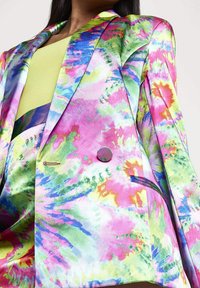 Acercamiento a una blazer de estampado tie-dye vibrante con tonos rosas, verdes, azules y amarillos, usada sobre un top acanalado verde lima.