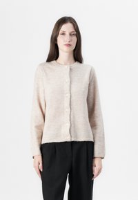 Lichtbeige, zachte gebreide cardigan met lange mouwen, ronde halslijn en zeven knopen aan de voorkant. De zoomlijn is iets cropped.