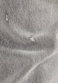 Tela de mezclilla gris con una textura suave, presenta pequeñas áreas deshilachadas, mostrando un diseño desgastado y sutiles variaciones en el color.