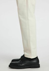 Pantaloni bianchi in cotone con un design a gamba dritta, abbinati a scarpe in pelle nere con lacci e suola in gomma.