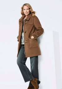 Brauner Wollmantel mit Kragen, Knopfverschlüssen und Taschen; kombiniert mit dunklen Jeans und braunen Ankle Boots. Der Mantel hat eine lockere Passform.