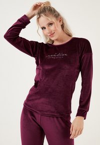 Burgundi sametist loungewear komplekt pikade varrukatega ja ümmarguse kaelusega. Ees on kontrastsetes värvides trükitud tekstidetail. Pehme, siidine tekstuur.