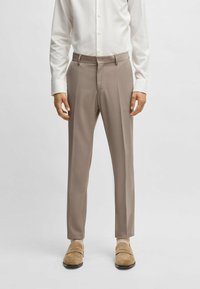 Pantaloni beige su misura con una leggera texture, caratterizzati da una parte frontale piatta, tasche laterali e passanti per cintura, abbinati a mocassini chiari.
