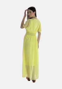 Robe maxi florale en jaune vif, avec de courtes manches bouffantes, une taille smockée et un tissu transparent qui descend jusqu'aux chevilles.