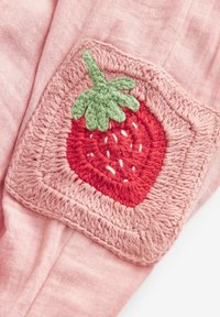 Patch carré au crochet avec fraise rouge et feuilles vertes sur un fond en tissu rose.