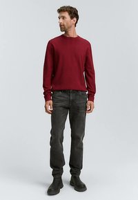 Rode gebreide trui, ronde hals, lange mouwen, gecombineerd met donkergrijze spijkerbroek en zwarte enkellaarzen. Eenvoudig ontwerp, gladde textuur.