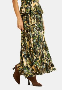 Gonna maxi floreale in verde, oro e nero con orlo volant. Abbinata a stivali alti in suede marrone. Tessuto leggero e fluido.