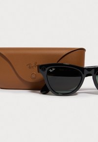 Gafas de sol negras Ray-Ban con lentes oscuros, que presentan una forma clásica de ojos de gato, junto a un estuche de cuero marrón.