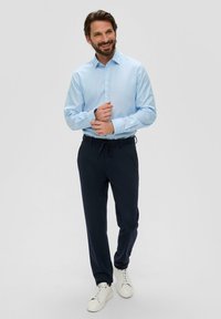Chemise bleu clair à manches longues avec des poignets boutonnés, associée à un pantalon à cordon de serrage bleu marine foncé. Des baskets blanches complètent la tenue.