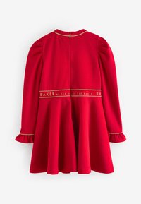 Sarkana kleita ar garām pūkainām piedurknēm, viļņotu aproču un platu svārku. Iekļauta zeltītā jostasvieta ar tekstu "BAKER by TED BAKER".