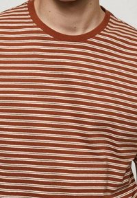 Camiseta de manga corta hecha de algodón, con una base color burdeos y franjas horizontales color crema. Cuello redondo con un ribete acanalado.