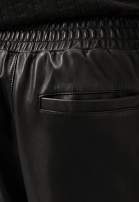 Schwarze Leder-Jogginghosen mit elastischem Bund, glatter Textur und einer kleinen Gesäßtasche mit rechteckiger Öffnung.