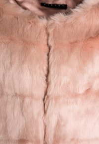 Chaleco de peluche rosa con una superficie suave y texturizada. Presenta una costura central y un escote redondeado. Sin cierres ni adornos visibles.