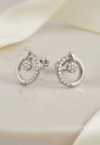 Sterlingsilverörhängen med cirkulära mönster, prydda med små klara ädelstenar och en sfärisk detalj, placerade på en ljus yta.