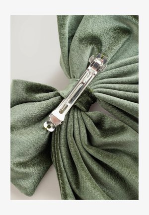 Grüner Samtband mit einem silbernen Metallverschluss, der eine weiche, strukturierte Oberfläche und Falten-Designdetails zeigt.