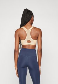 Sostenes deportivos beige con un diseño de espalda nadadora y un detalle de corte circular en la parte posterior, combinados con leggings de tiro alto en color marino.