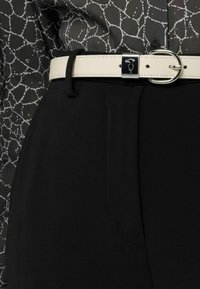 Czarne spodnie o gładkiej fakturze i prostym kroju. Całość dopełnia biały skórzany pasek z srebrną klamrą oraz wzorzysta szara bluzka.