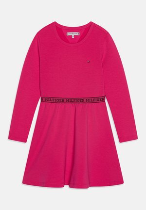 Sukienka z długim rękawem w jasnoróżowym materiale, z okrągłym dekoltem i marszczoną spódnicą. Czarny pas w talii z napisem „HILFIGER”.