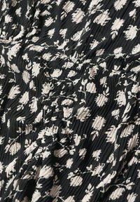 Tissu noir avec motif floral blanc et texture froncée et froissée créant de petites crêtes surélevées à la surface.