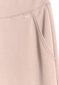 Gros plan d'une poche en tissu beige avec coutures renforcées et petite étiquette métallique rectangulaire de marque près de la couture.