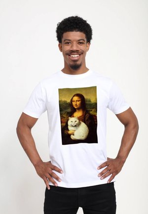 Uomo sorridente con le mani sui fianchi che indossa una maglietta bianca con la riproduzione della Mona Lisa che tiene un gatto bianco su sfondo semplice.