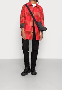 Rød ternet oversized skjorte med sorte accenter, parret med sorte bukser og kraftige sorte støvler. Lille crossbody taske hængende over skuldrene.