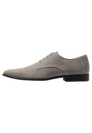 Chaussure habillée en daim gris pour homme avec laçage fermé, bout pointu et talon bas noir sur fond blanc.