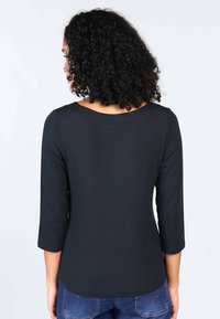Black long-sleeve top with a rounded neckline, smooth texture, and three-quarter sleeves, paired with blue denim jeans.