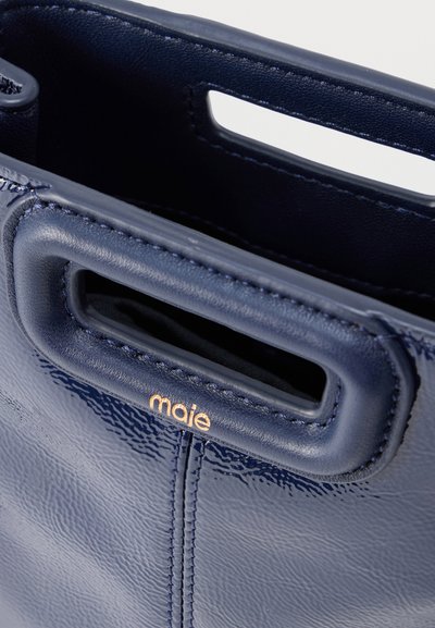 Δερμάτινη τσάντα σε ναυτικό μπλε χρώμα με λεία υφή, διαθέτει ορθογώνια λαβή κομμένη και ανάγλυφο λογότυπο "maie" σε χρυσό.
