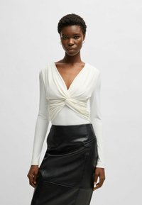 Top bianco a maniche lunghe con un design frontale annodato abbinato a una gonna in pelle nera a vita alta caratterizzata da una texture liscia e tasche sottili.