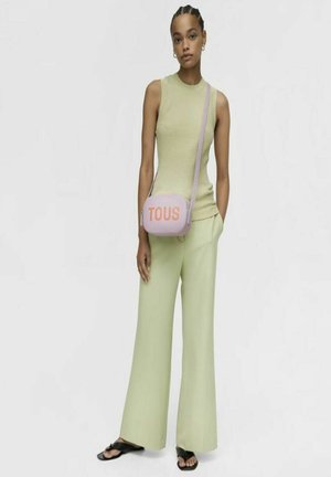 Top sin mangas de color verde claro con texturizado en canalé, pantalones de pierna ancha de color verde claro y un bolso rosa con el logo "TOUS" en naranja. Sandalias planas negras.