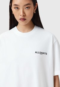 Λευκό βαμβακερό t-shirt με στρογγυλή λαιμόκοψη, κοντά μανίκια και μαύρο λογότυπο "ALLSAINTS LONDON" στην αριστερή πλευρά του στήθους.