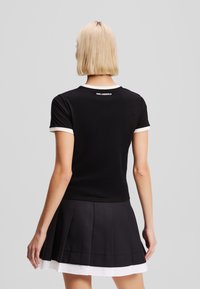 Black cotton T-shirt with white ribbed collar and cuffs, featuring a logo on the back. Paired with a pleated black skirt with white accents.