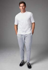 Camiseta blanca de jersey y pantalones de chándal grises, combinados con zapatillas deportivas negras. El conjunto presenta un diseño casual y ajustado, y una textura suave.