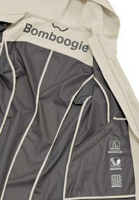 Giacca beige idrorepellente con fodera grigia, presenta il logo "Bomboogie", tasche con zip e icone che indicano le qualità antivento e traspirante.