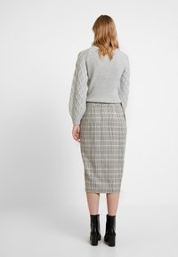 Pull en maille grise avec des manches texturées en tricot à torsades, associé à une jupe crayon à carreaux et des bottines à talons noirs.