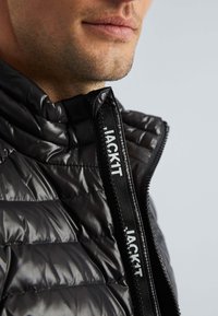 Zwarte gewatteerde jack met een glanzende, gestikte textuur, voorzien van een hoge kraag en een rits aan de voorkant met een merk pull tab.