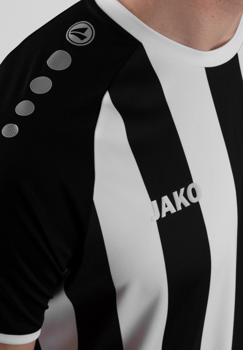 Maillot de sport rayé noir et blanc avec un col rond, présentant un logo sur l'épaule et des accents circulaires le long de la manche.