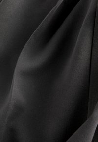 Schwarzer Stoff mit glatter Textur und leichtem Glanz, der mit weichen Drapierungen sanfte Falten und Kurven im Material erzeugt.