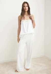 Top sin mangas blanco y ligero con un borde de encaje, combinado con pantalones blancos anchos y holgados. Tejido suave, textura lisa, diseño minimalista.