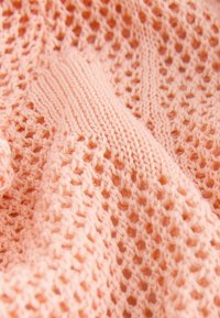 Gros plan d'un tissu tricoté doux couleur pêche avec un motif de maille ouverte et des mailles côtelées solides.
