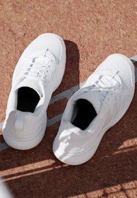 Coppia di scarpe da ginnastica bianche con lacci lasciate su una pista rossa vicino a una linea bianca che segna la corsia.