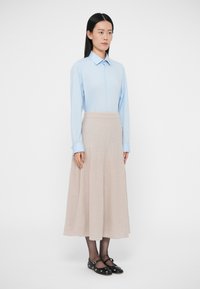 Vaaleansininen nappipaita pitkillä hihoilla, yhdistetty beigenväriseen, levenevään polvipituiseen hameeseen. Mustat kengät, joissa on hihnallinen yksityiskohta.