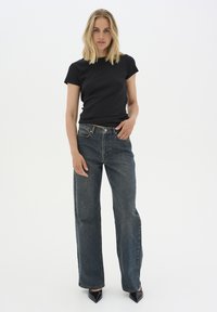 Svart figurnära t-shirt tillsammans med högmidjade, vida mörkblå jeans i denim. Bärs med spetsiga svarta klackar; enkel och minimalistisk design.